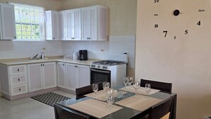 Una cocina moderna con alacenas blancas, una estufa a gas y un comedor con mesa puesta para cuatro.