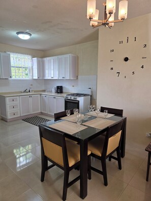 A modern kitchen with white cabinets, a gas stove, and a dining area with a table set for four. - Ajani - Cozy 2 Bedroom 1 Bath Apt next beach and activities, sleeps 4  (Oistins)