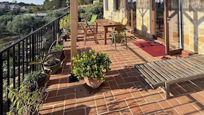 Une terrasse couverte avec une table et des chaises, des plantes en pot et une vue sur le paysage environnant.