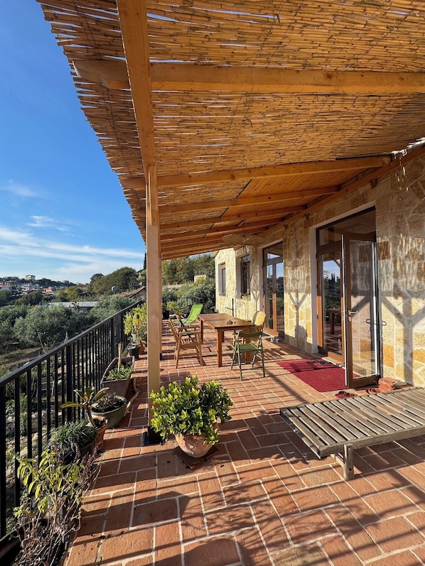 Une terrasse couverte avec une table et des chaises, des plantes en pot et une vue sur le paysage environnant.