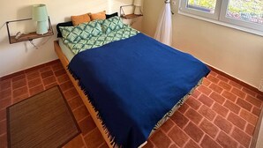 Une chambre à coucher avec un lit, un luminaire suspendu, une œuvre d’art murale et une fenêtre avec des rideaux.