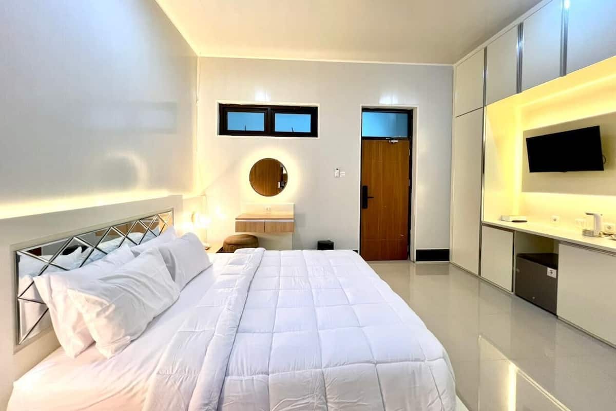 A modern bedroom with a large bed, a bedside table, a mirror, and a TV mounted on the wall.