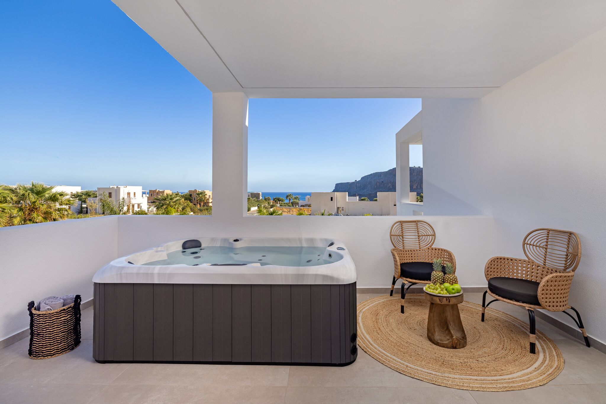 A balcony with a hot tub, wicker chairs, and a woven rug.