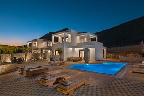 Una casa moderna con piscina, area salotto esterna e un muro in pietra.