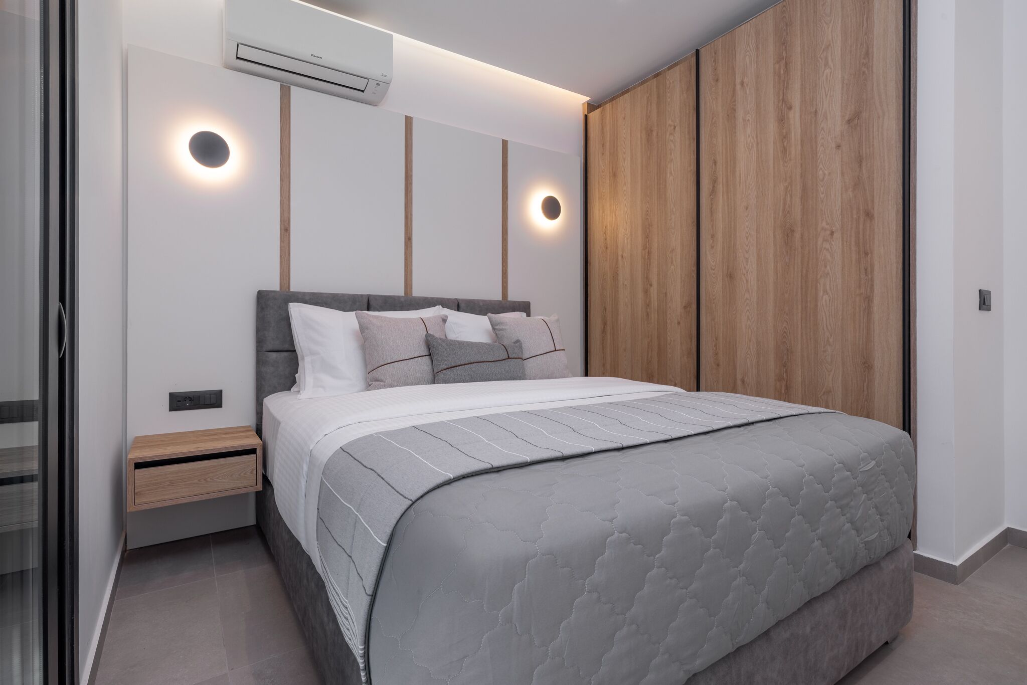 A modern bedroom with a large bed, built-in nightstands, and a wooden wardrobe.