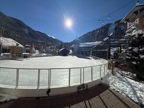 A snow-covered outdoor area with a circular viewing platform, buildings in the background, and a clear sky. - Cozy Mountain Condo Steps from the Main Lift (Taos Ski Valley)