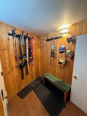 Une pièce servant de local à skis, avec des skis et des casques rangés sur des étagères, un banc et une porte.