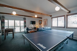 A room with a ping pong table, a sofa, a television, and a window with a view. - Cozy Mountain Condo Steps from the Main Lift (Taos Ski Valley)