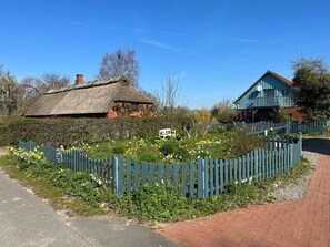 Un cadre rural avec une maison à toit de chaume, une clôture en bois et un chemin pavé de briques.