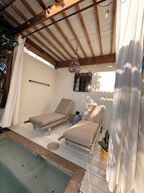 A sunlit outdoor lounge area with two lounge chairs, a small table, and a hanging light fixture. - Private Pool Suite with outdoor tub in Rincon (Rincón)