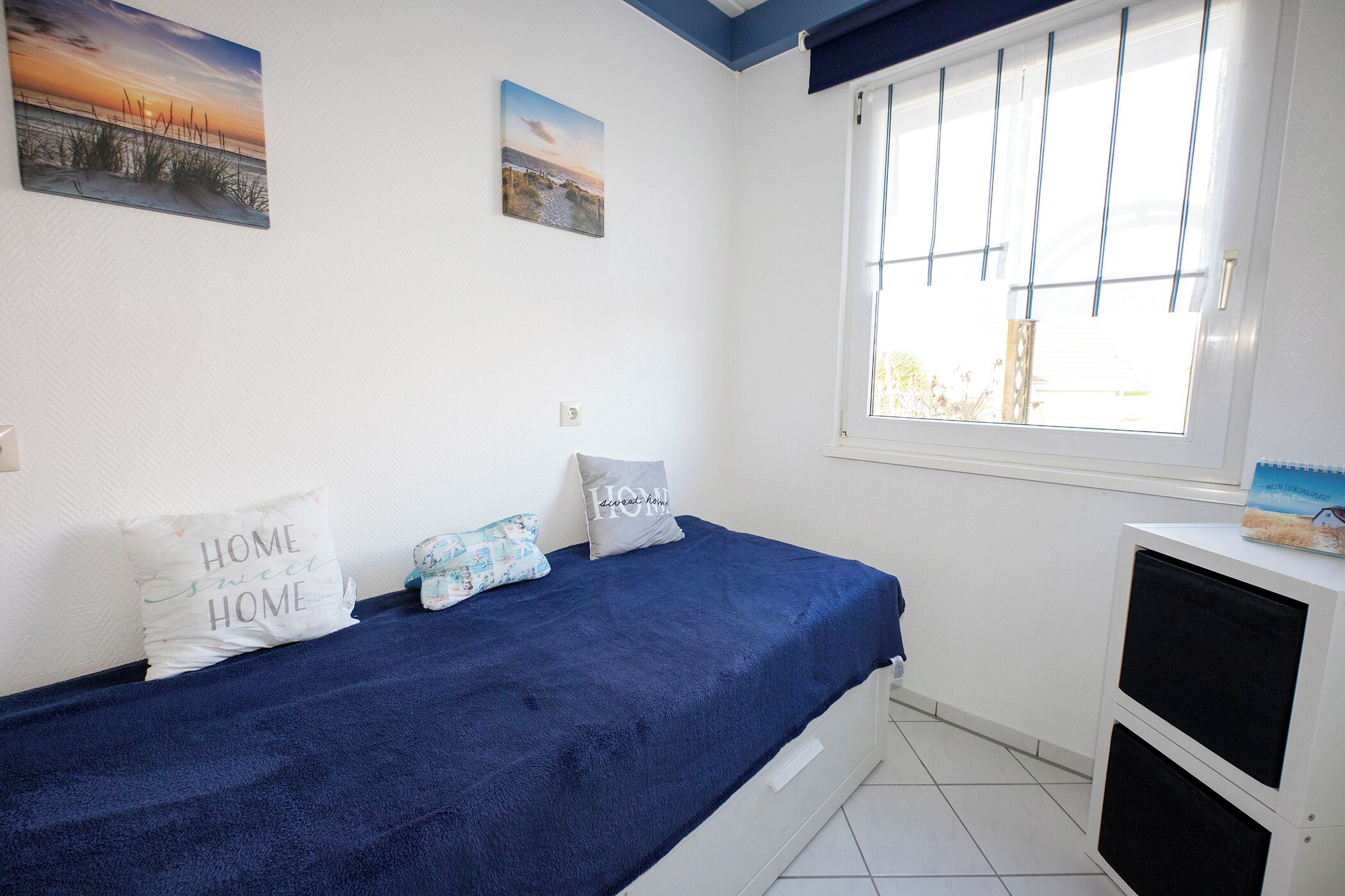 A bedroom with a bed, pillows, a window, and a small cabinet.