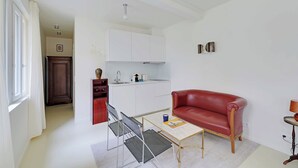 A compact living space with a kitchenette, a red leather sofa, a small table, and a chair. - Cozy Studio 2P - Montmartre (Paris)