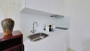 A modern kitchen with a stainless steel sink, a toaster, and a vase with dried plants on a wooden shelf. - Cozy Studio 2P - Montmartre (Paris)
