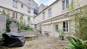 A courtyard with a cobblestone floor, potted plants, and a covered object. - Cozy Studio 2P - Montmartre (Paris)