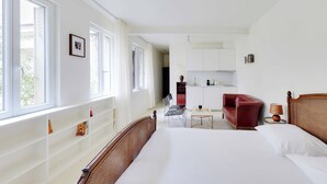 A hotel room with a large bed, a desk, a chair, and a red sofa. There is a kitchenette in the background. - Cozy Studio 2P - Montmartre (Paris)