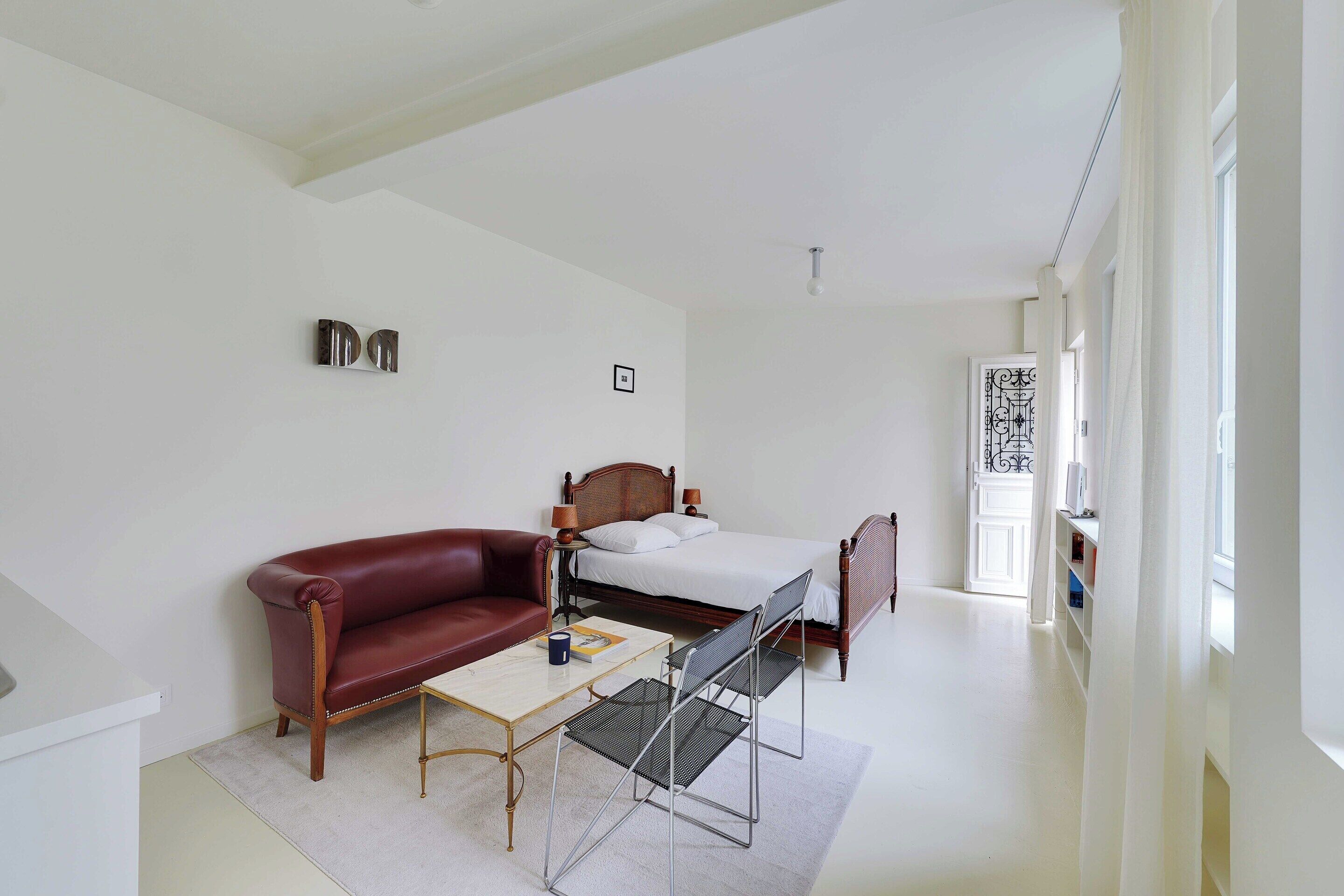Une chambre d’hôtel avec un lit, un canapé en cuir rouge, une petite table et une chaise.