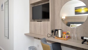 A modern hotel room with a flat-screen TV mounted on a wooden wall, a round mirror, a coffee machine, and a tray with breakfast items.