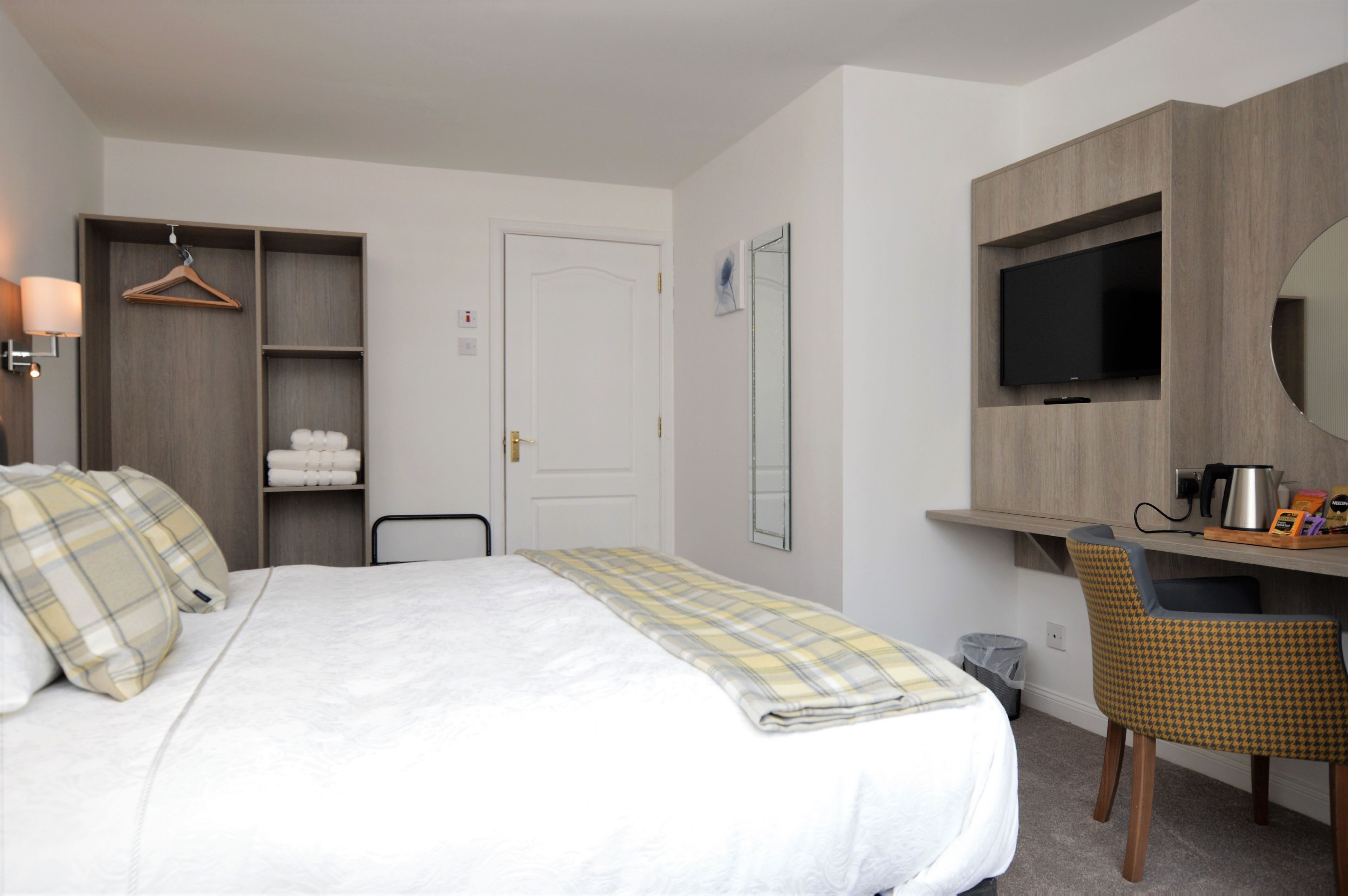 Una camera d'albergo con un letto, una scrivania con una sedia, una televisione e uno specchio.