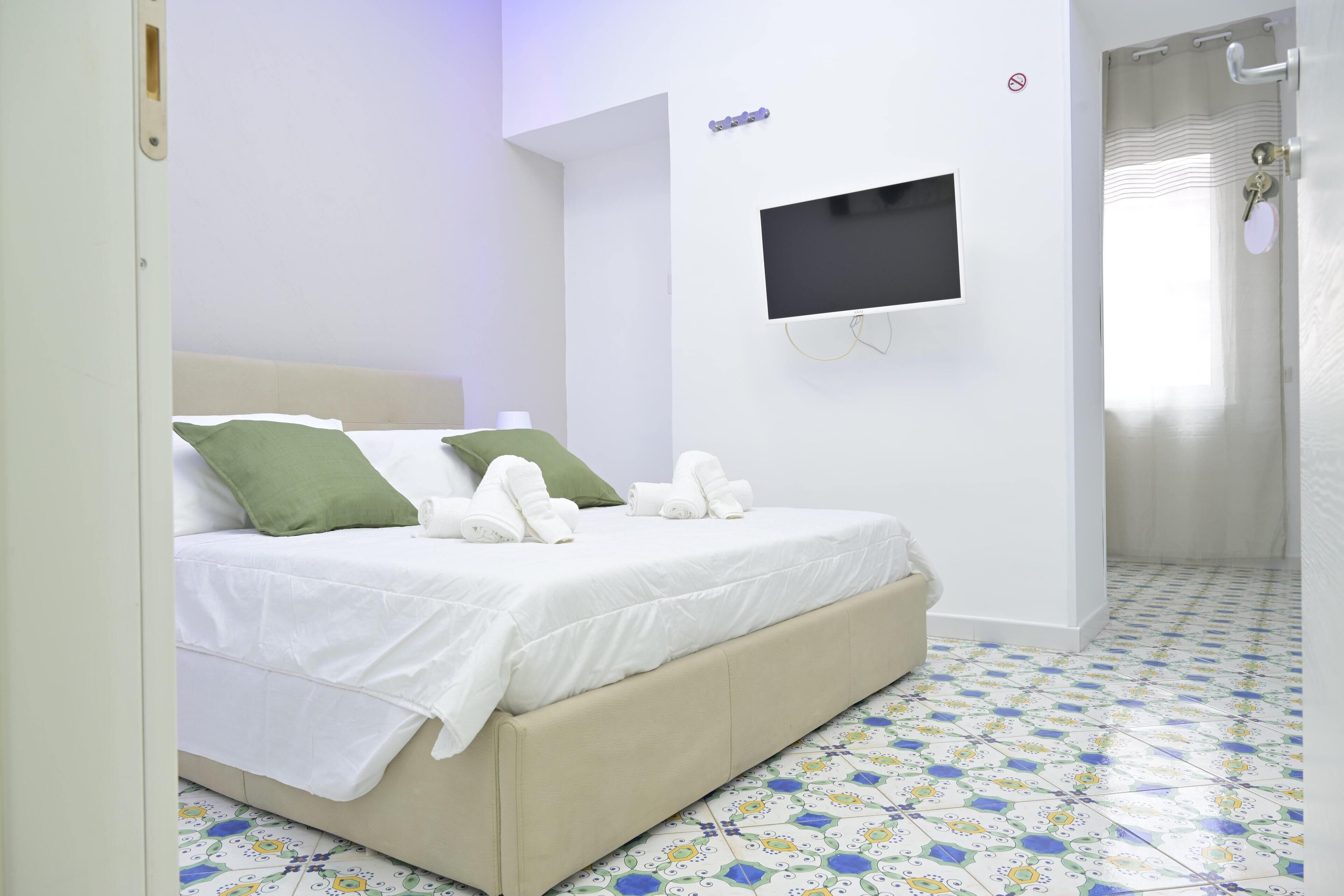 Un dormitorio con cama, televisor montado en la pared y baño con cortina de ducha.