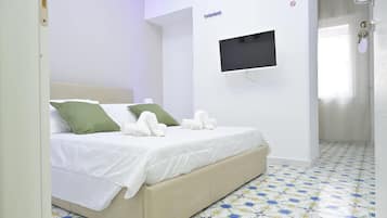 Un dormitorio con cama, televisor montado en la pared y baño con cortina de ducha.