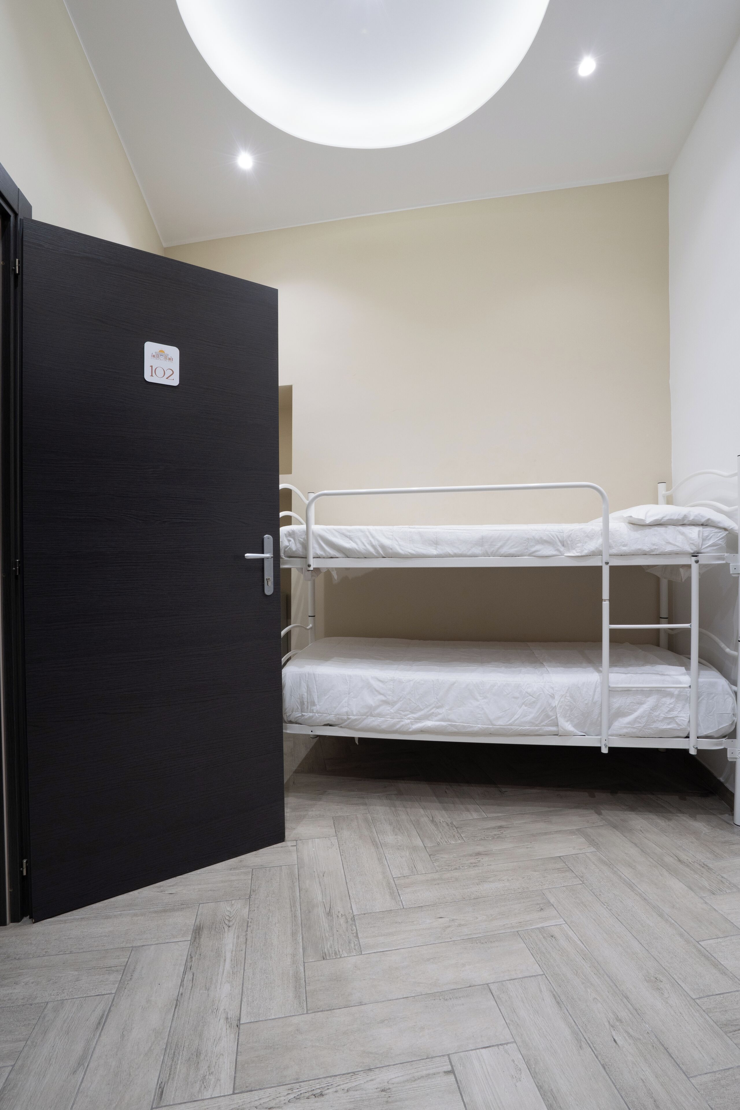 A room with a bunk bed, a black door, and a herringbone-patterned floor.