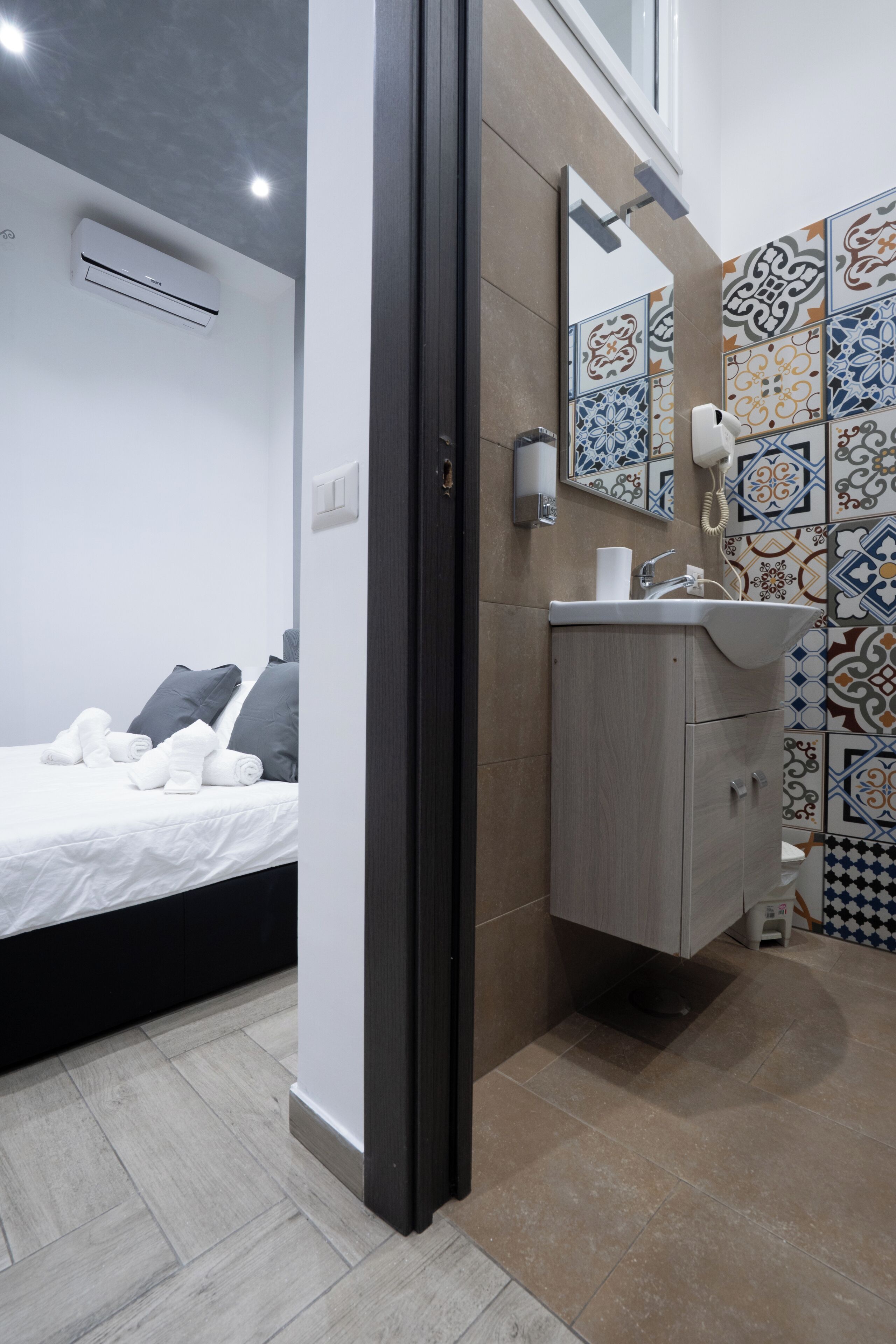A modern hotel room with a bed, a bathroom with a sink and mirror, and a decorative tile wall.