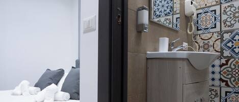 A modern hotel room with a bed, a bathroom with a sink and mirror, and a decorative tile wall.