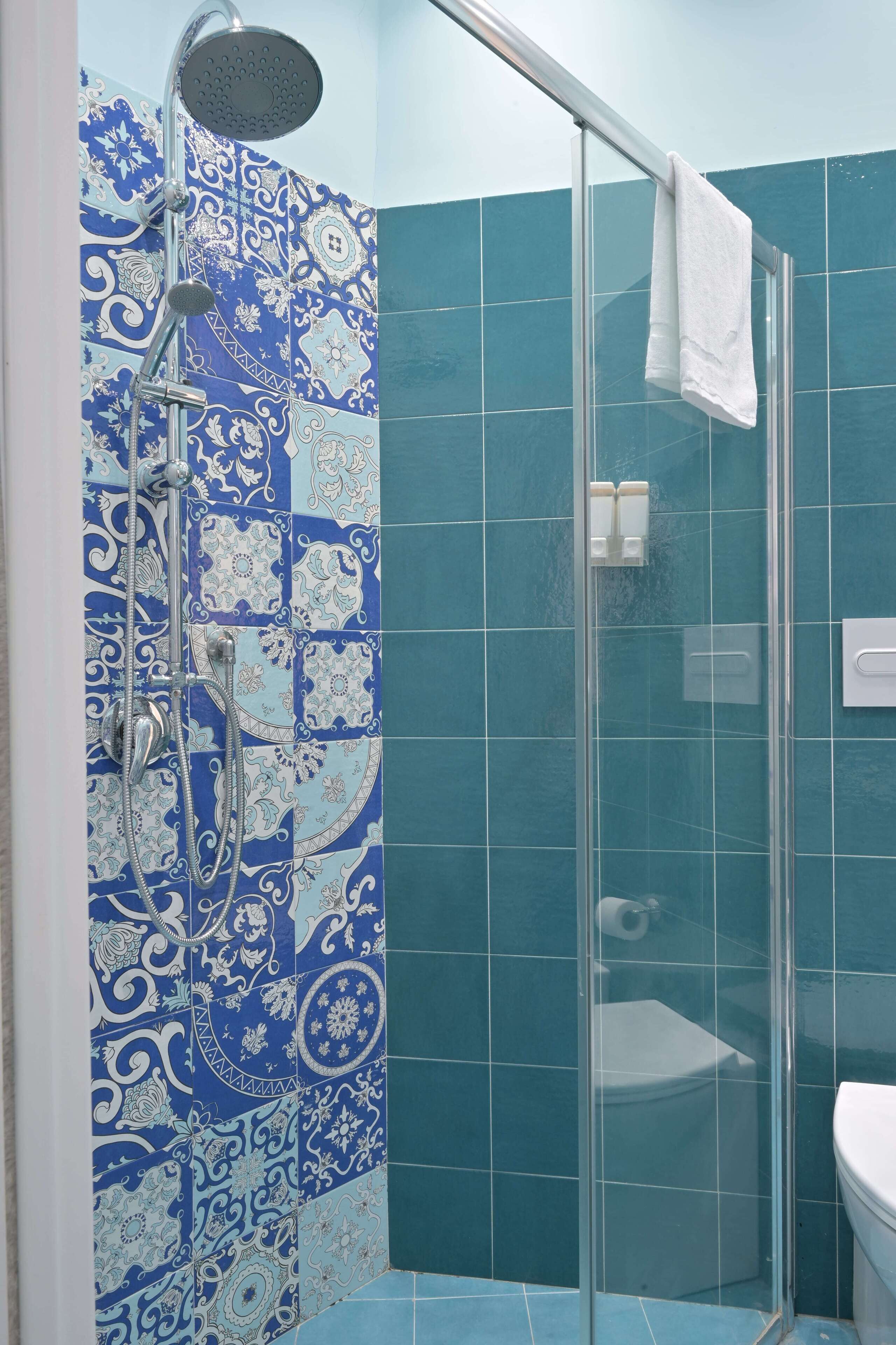 Un baño con ducha, puerta de vidrio y azulejos de diseño azulado.