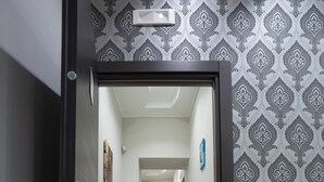 A hallway with patterned wallpaper, a wooden floor, and a white lamp on a cabinet. - La dimora del Sole (Ercolano)