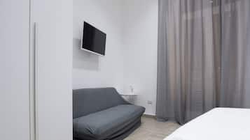 A modern bedroom with a bed, a sofa, a TV, and a window with sheer curtains.