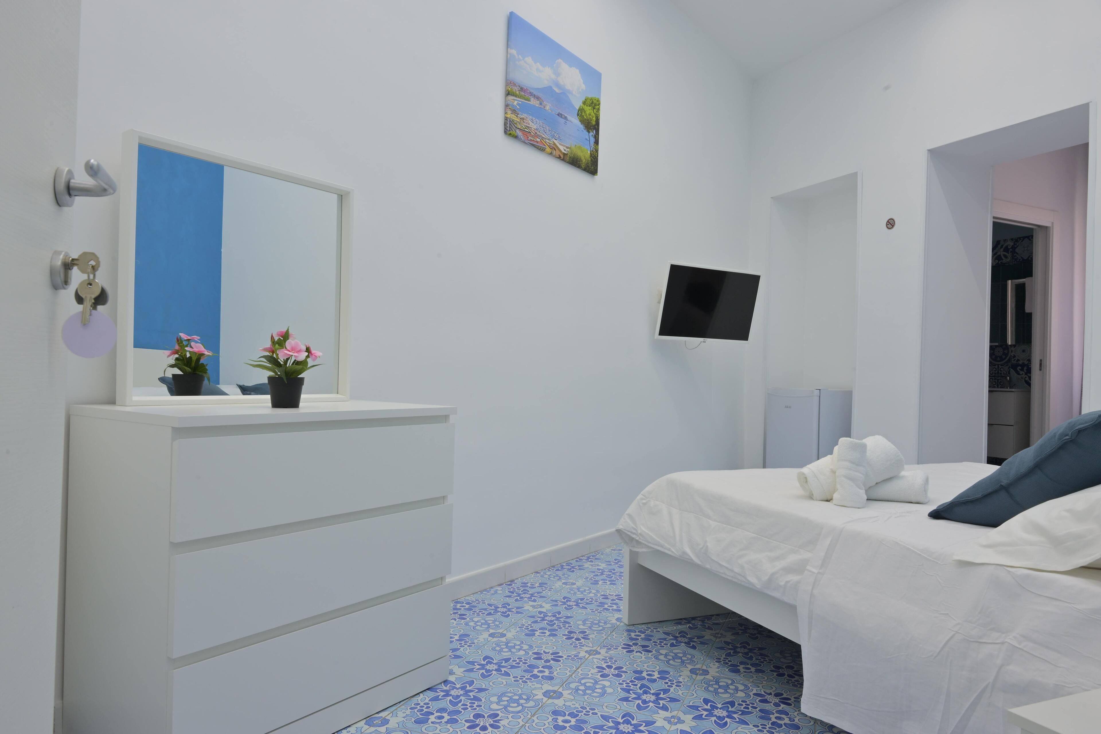 A bedroom with a bed, a dresser, a TV, and a painting on the wall.