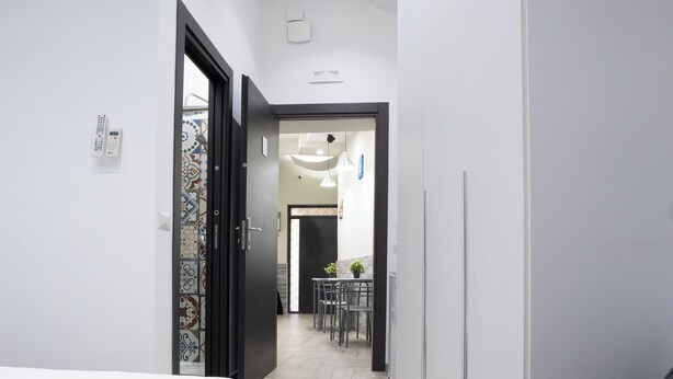 A narrow hallway with a bed on the left and a sofa on the right, leading to a dining area with chairs and a table. - La dimora del Sole (Ercolano)