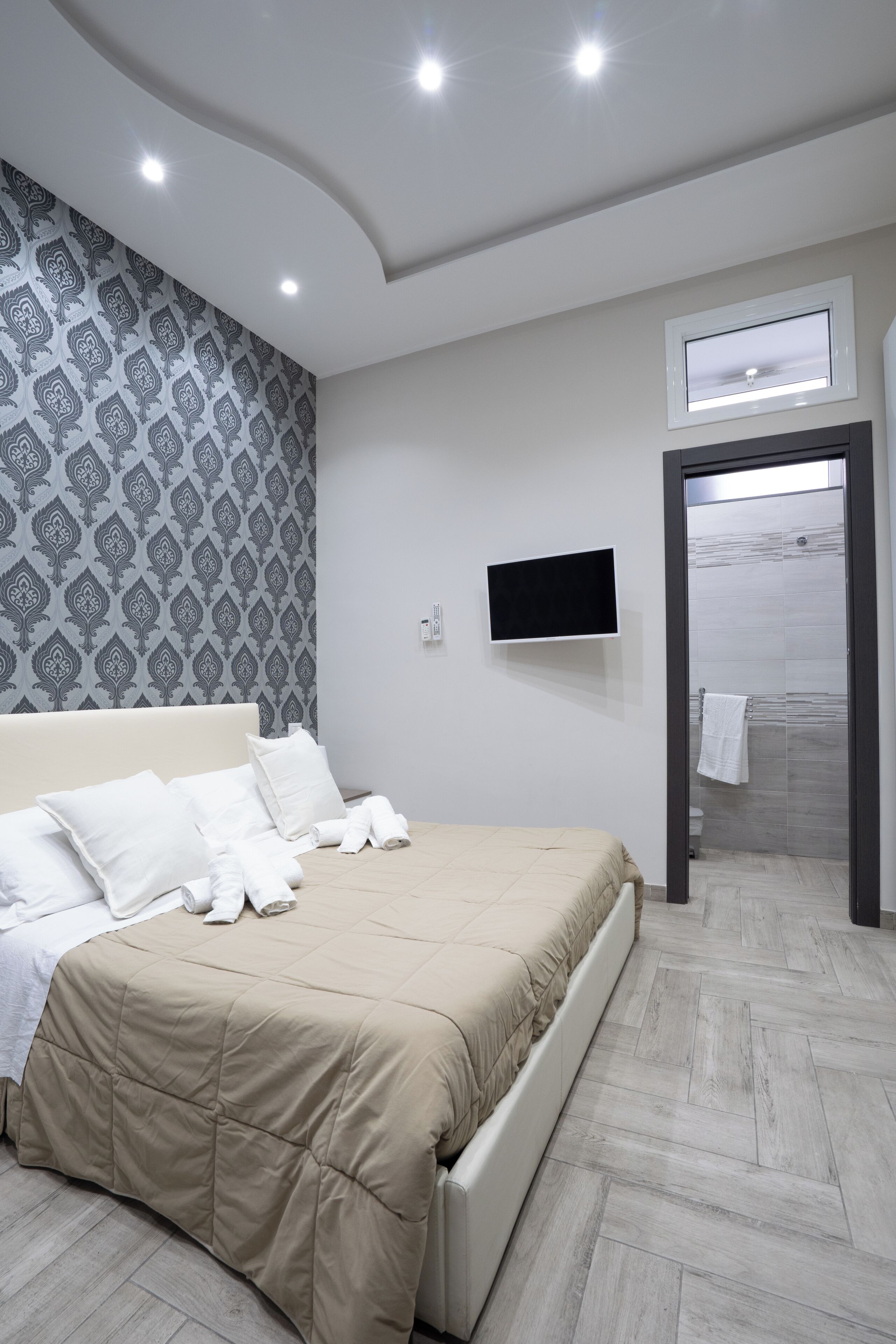 A modern hotel room with a large bed, a flat-screen TV, and a shower area visible through an open door.