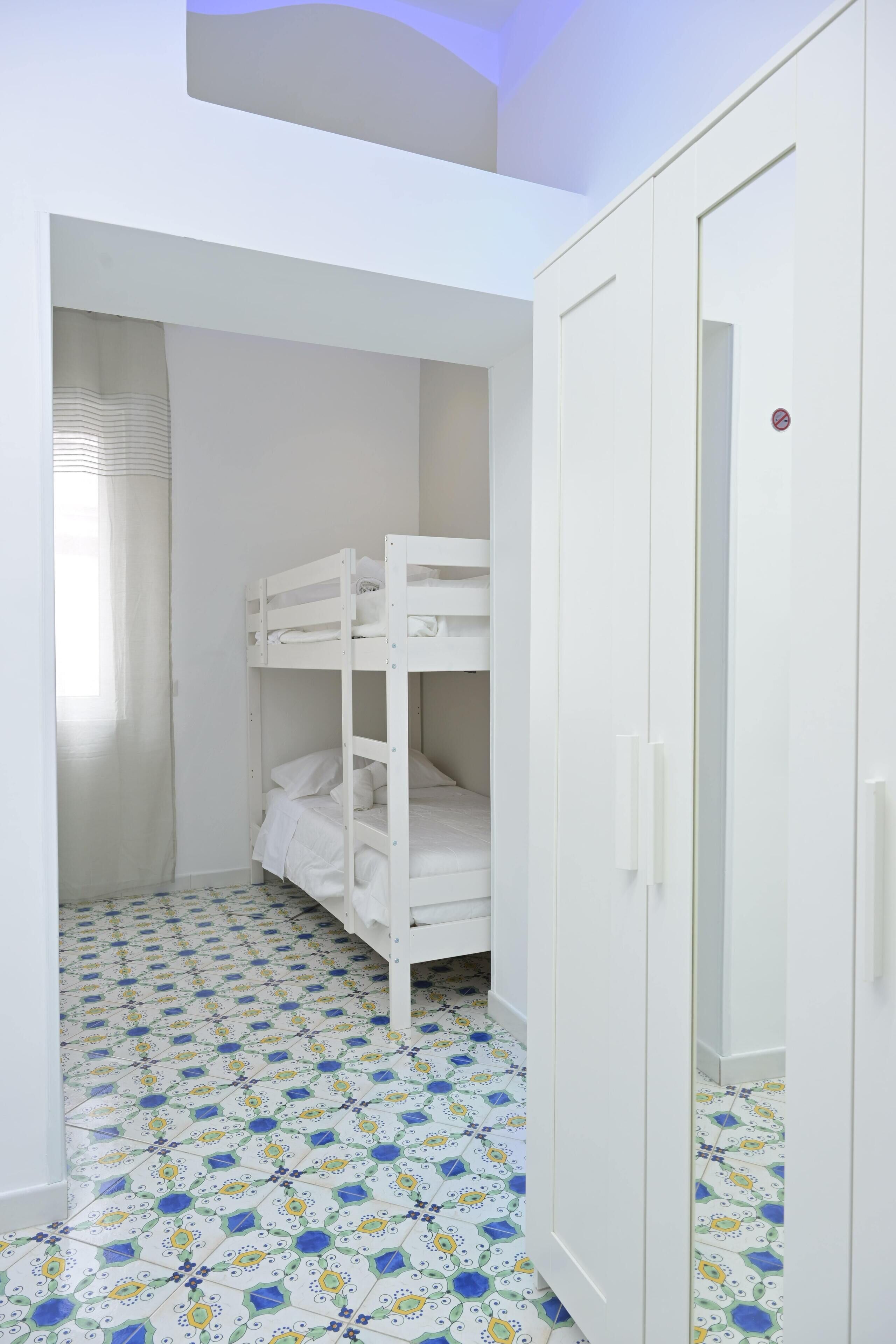 A room with bunk beds, a wardrobe, and patterned floor tiles.