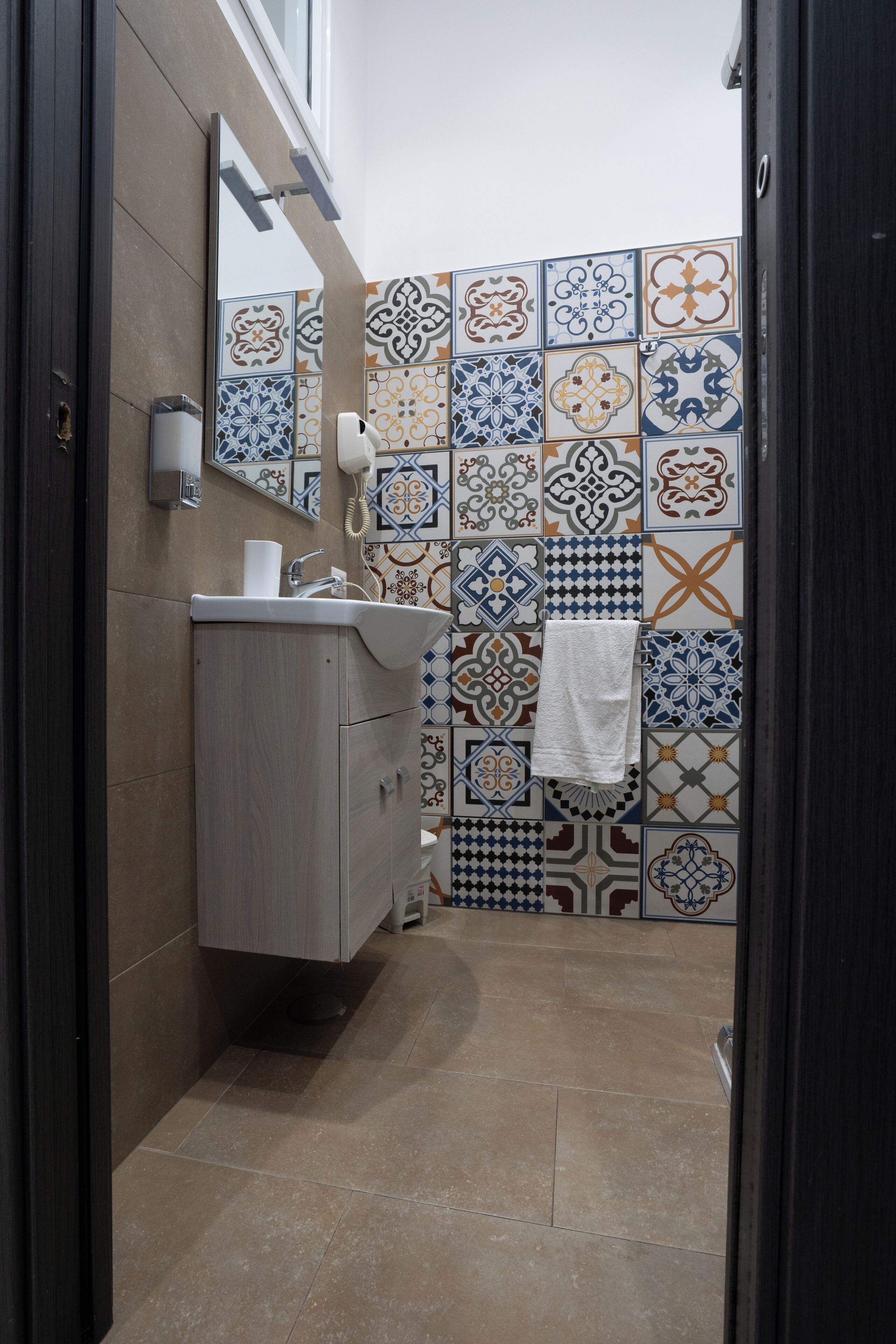 A bathroom with a sink, mirror, and patterned tiles on the walls.