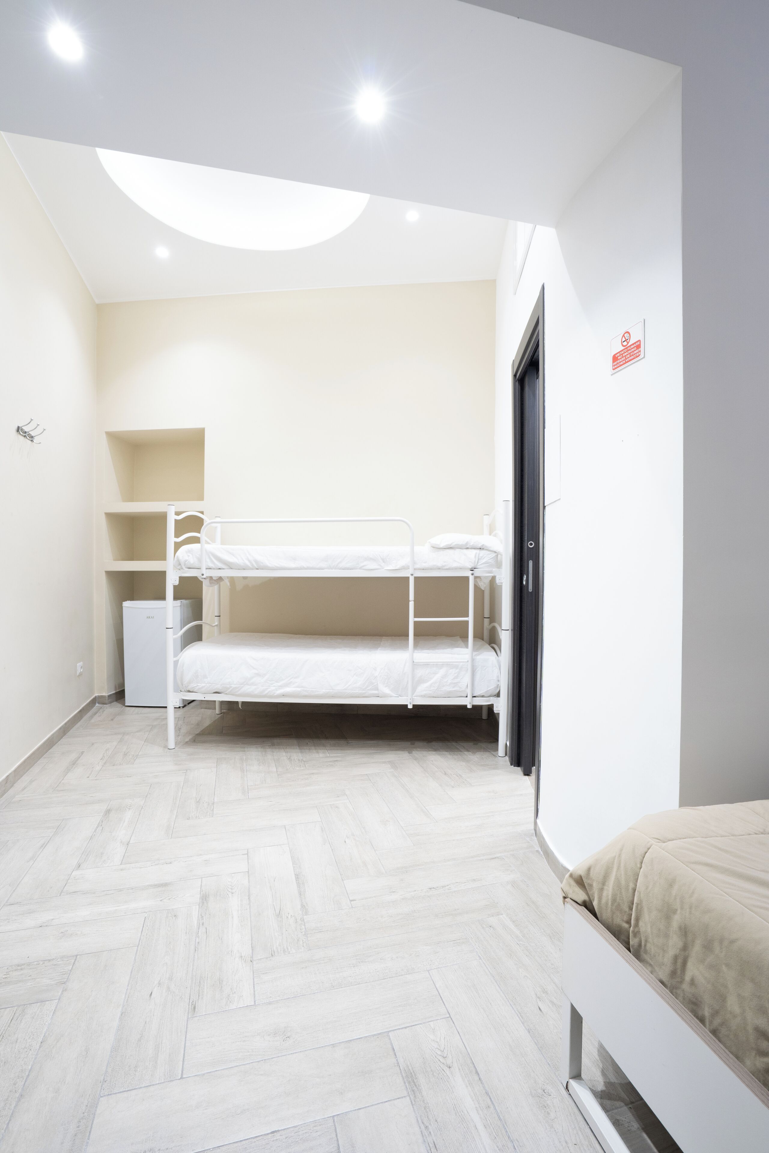A bunk bed room with a white ceiling, a small white cabinet, and a door with a red sign.