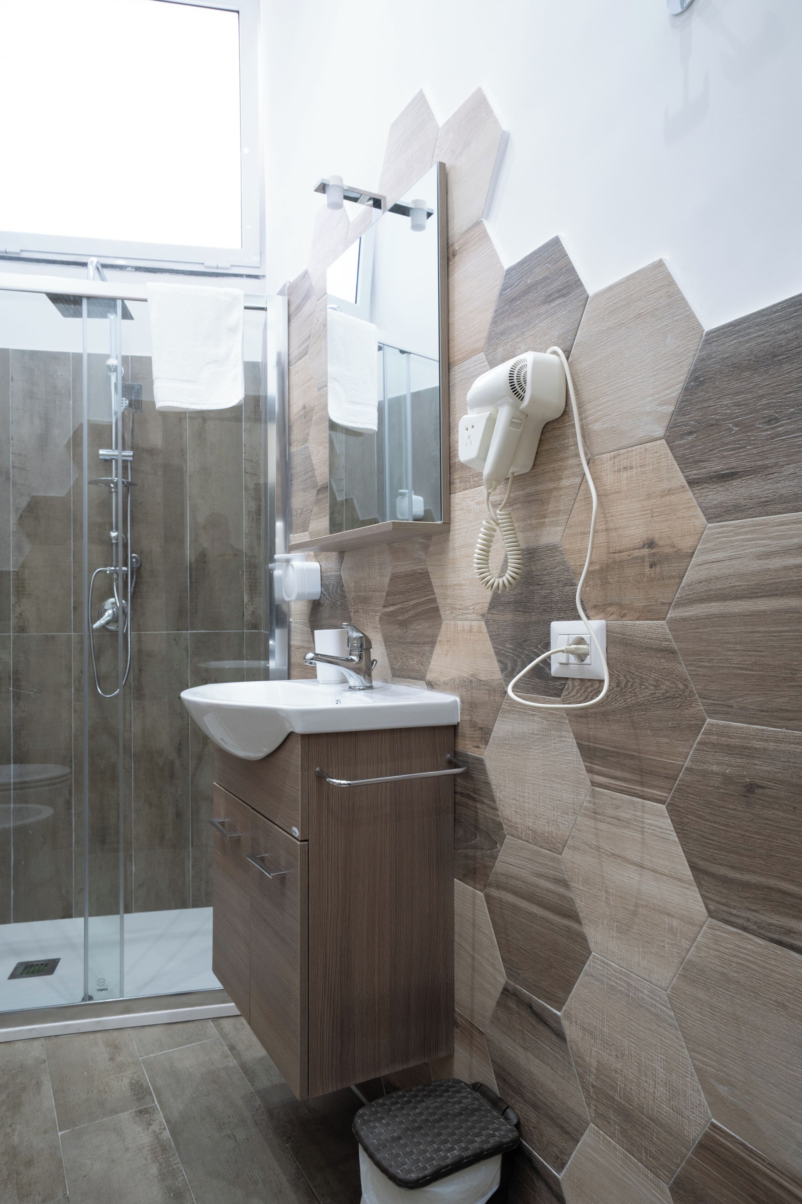 Un baño moderno con cabina de ducha de vidrio, tocador de madera y espejo con secador incorporado.