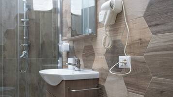Un baño moderno con cabina de ducha de vidrio, tocador de madera y espejo con secador incorporado.