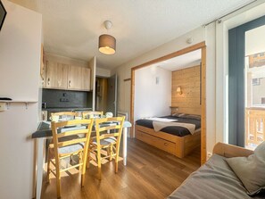 Ein kompaktes Zimmer mit Küchenzeile, einem Essbereich mit Tisch und Stühlen, einem Bett mit Holz Kopfteil und einem Fenster mit Blick.