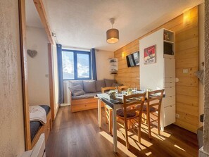 Ein gemütliches Blockhaus mit Holzvertäfelung, einem Essbereich mit Tisch und Stühlen, einem Sofa, einem an der Wand montierten Fernseher und einem Fenster mit Bergblick.