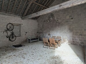 A rustic room with a stone wall, a wooden bench, a table with chairs, and a bicycle leaning against the wall.