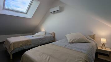 Une petite chambre confortable avec deux lits, une lucarne, un climatiseur et une lampe de chevet.