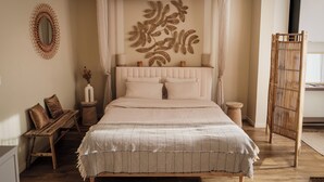 Een slaapkamer met een hemelbed, een houten bankje, een spiegel en een decoratief wandobject.