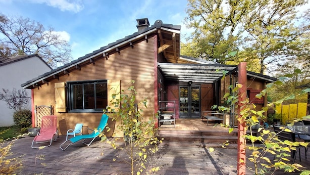 A wooden house with a covered patio, two blue chairs, and a small garden area.