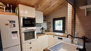 A compact kitchen with white cabinets, a microwave, oven, and a sink.