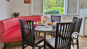 A dining area with a red bench and four wooden chairs around a table set with breakfast items. - Bright Gîte near Laval, 3 bedrooms, large grounds, ideal for families (L'Huisserie)