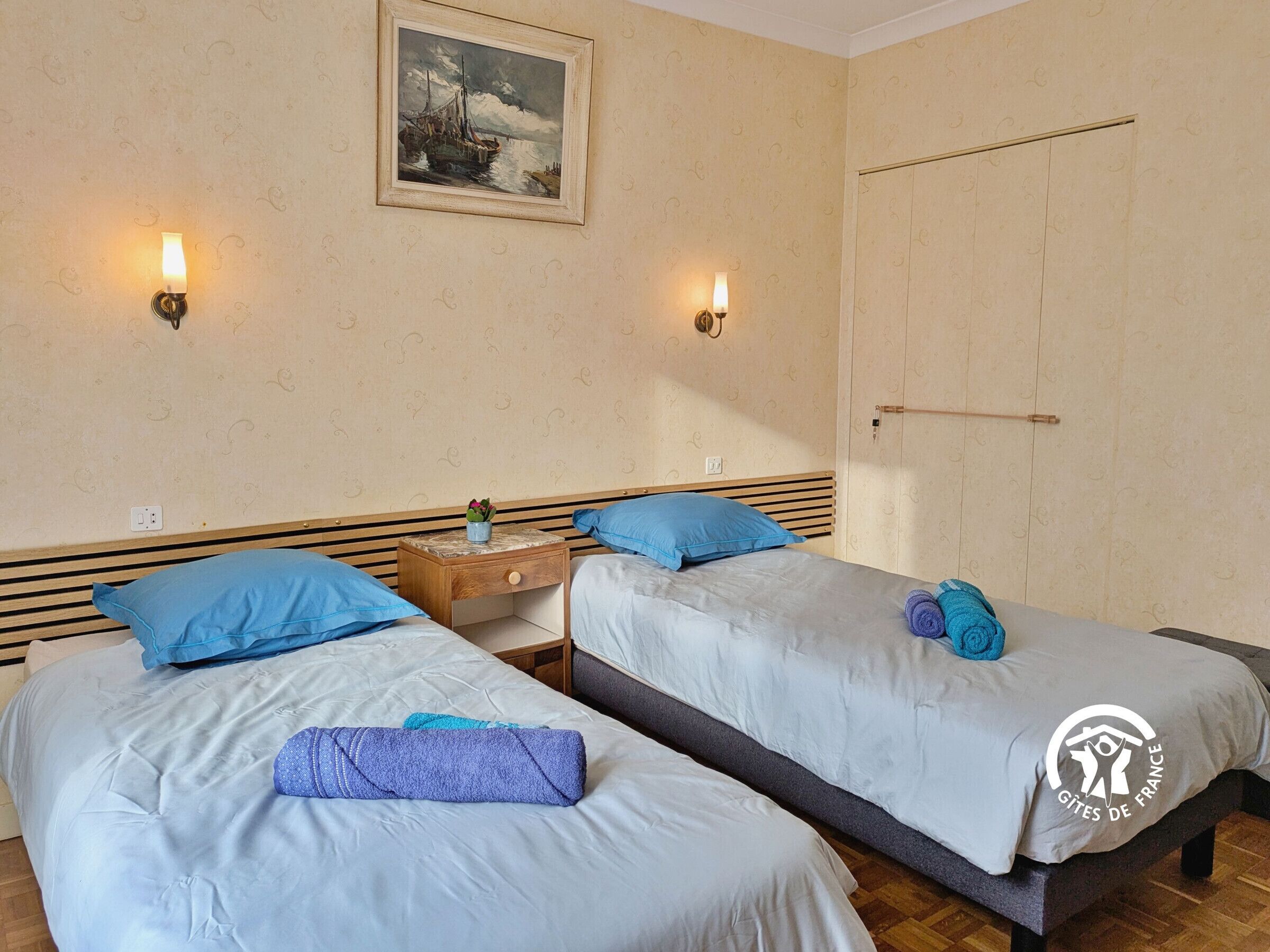 A hotel room with two beds, a nightstand, a painting on the wall, and a wardrobe.