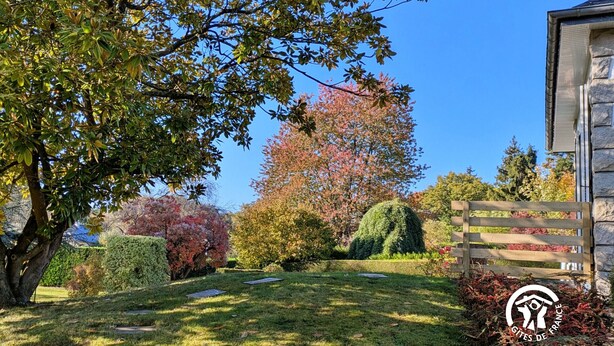 A well-maintained garden with a variety of trees, a wooden fence, and a stone building. - Bright Gîte near Laval, 3 bedrooms, large grounds, ideal for families (L'Huisserie)
