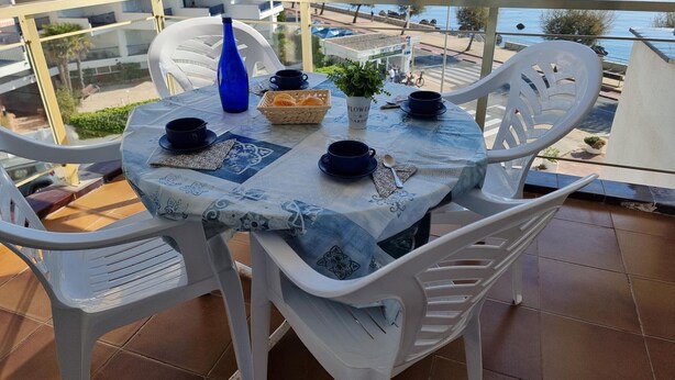 A round table with a blue and white patterned tablecloth, white plastic chairs, and a blue vase. - Comfortable apartment with terrace 200m from the beach (L'Escala)