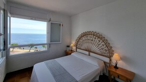 A bedroom with a bed, a window with a view of the sea, a decorative headboard, and bedside lamps. - Comfortable apartment with terrace 200m from the beach (L'Escala)